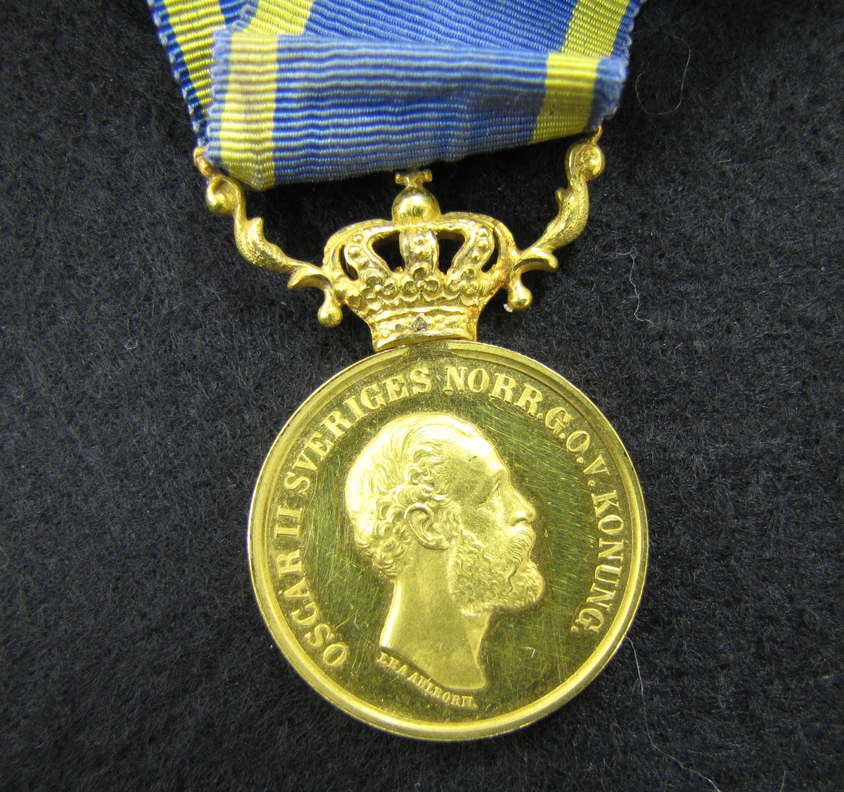 Medalj med blågult band. Medaljen är av 5:e storleken i sitt numera mycket sällsynta originaletui, utdelad 1880 till Lotsen Johan Fredrik Kafvelström (1823-10-03 - 1899-02-07) i Vänersborg. 

Medaljen är av 23 K guld och krona och bärornament av 18 K guld och monterat med sitt originalband vilket Kafvelström av bevarade fotografier bar monterat i en rosett, viket normalt endast brukas av damer.

Medaljen "För berömliga gärningar" instiftad 1803 men kom först till användning 1842 då storlekarna 8 & 5 infördes. Medaljen utdelades i såväl guld som silver. Vilken av dem räddningsmannen tilldelades berodde givetvis på bragdens betydelse och i vilken livsfara även den räddande och den räddade befunnit sig vid olyckan. Den räddandes sociala ställning hade även, märkligt nog, betydelse för vilken av de olika storlekarna som utdelades.

X På framsidan: Oskar II:s bild. På frånsidan: Berömliga gerningar till J F Kafvelström Lots

Bilagor: VM 16978
Tidningsklipp, foto av Lotsen J F Kafvelström, intervju med Arndt Winberg (barnbarn till Kafvelström), bandinspelning.

Släktingarna till Losten J. F Kafvelström. Barnbarn: Arndt, Anna-Greta, Karin och John Winberg, Uddevalla, Barnbarns barn: Frank Larsson, Vänersborg.