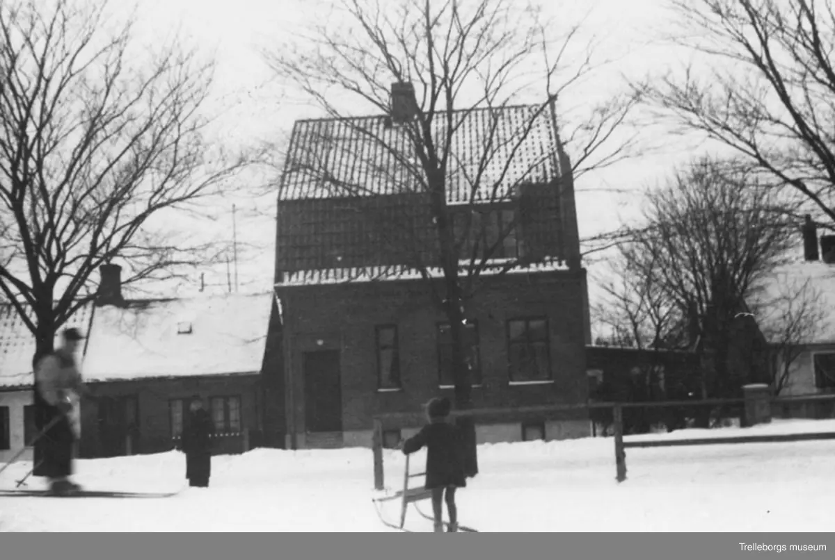 Boningshus utmed Valldammsgatan inom kv. Alsingehejdan i Trelleborg på vintern 1964. I förgrunden en flicka som åker spark. Här låg senare arbetsförmedlingen.