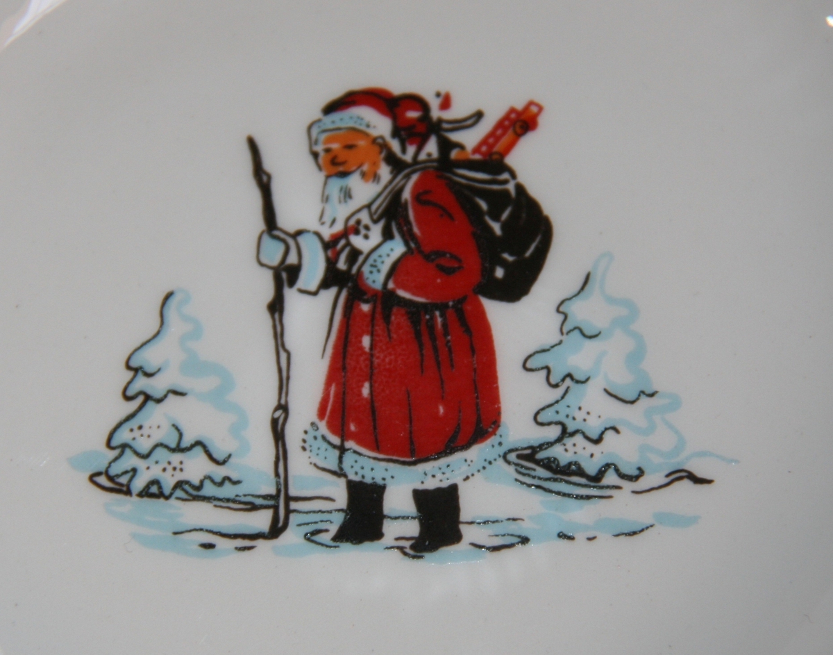Motiv med nisse med stav og gavesekk på ryggen som går i snøen.  I tillegg har kopp på andre siden motiv av ei hytte/hus i skogen/på fjellet.