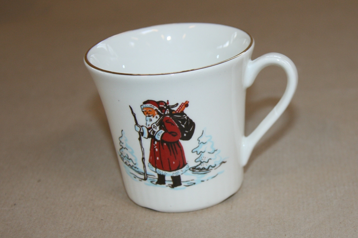 Motiv med nisse med stav og gavesekk på ryggen som går i snøen.  I tillegg har kopp på andre siden motiv av ei hytte/hus i skogen/på fjellet.