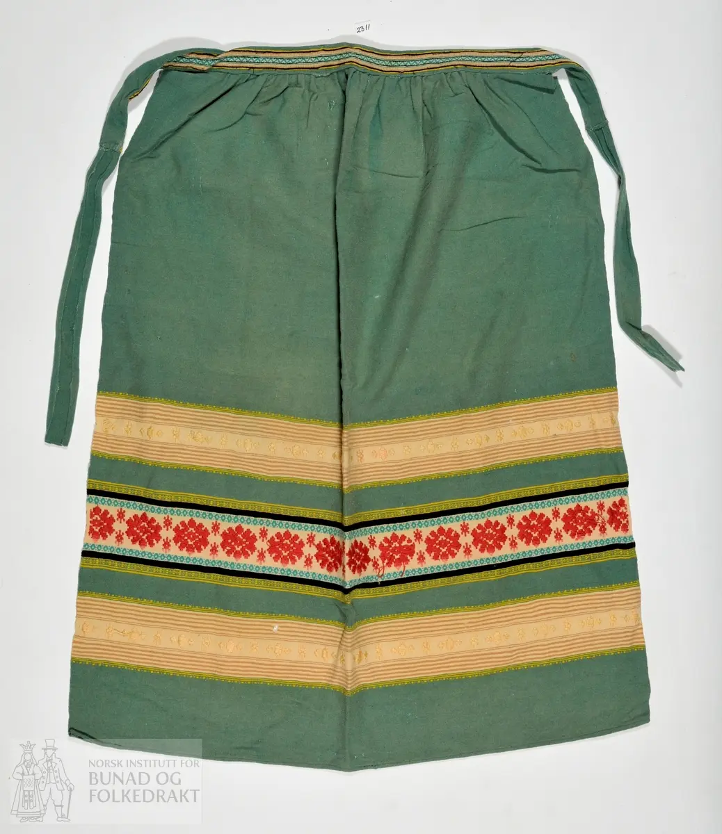 Grønt forkle, truleg i blandingskvalitet med border i ulike fargar. Mønstervove i stripene, ellers ein lerretsbinding. 
- 77 cm lengde. 64 cm breidde. 40 cm breidde i livet.