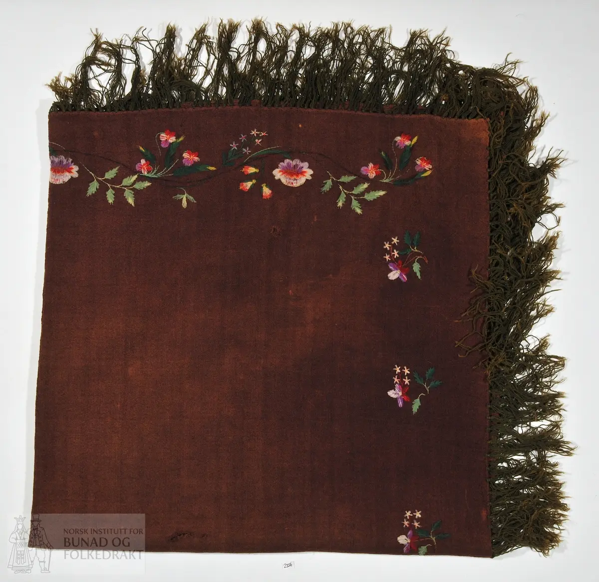 Sjal i burgunder, kypertvevd ullstoff med påknytte frynser av tre-tråders ullgarn. Sjalet er brodert langs kantene med blomsterranker og buketter. Sjalet kan ha to ulike sider, der den ene er mer utbrodert og i lysere farger. Plattsøm, attersting og sjattersøm. Brodergarn i ull.

Opprinnelig fra Meringsdalen i Murudalen, gitt til nåværende eires bestemor etter arbeid med bakst på gården.