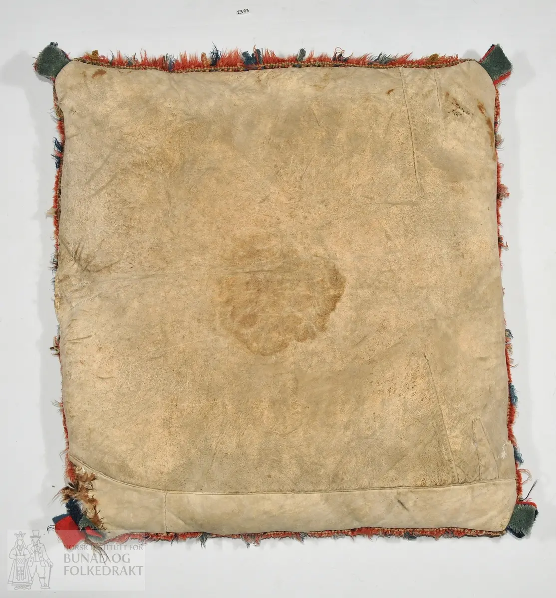 Pute av vevd ullsstoff etter billedvevprinsippet i ulike farger. Skinn på baksida. Fora med fjør og dun. 60 x 60
