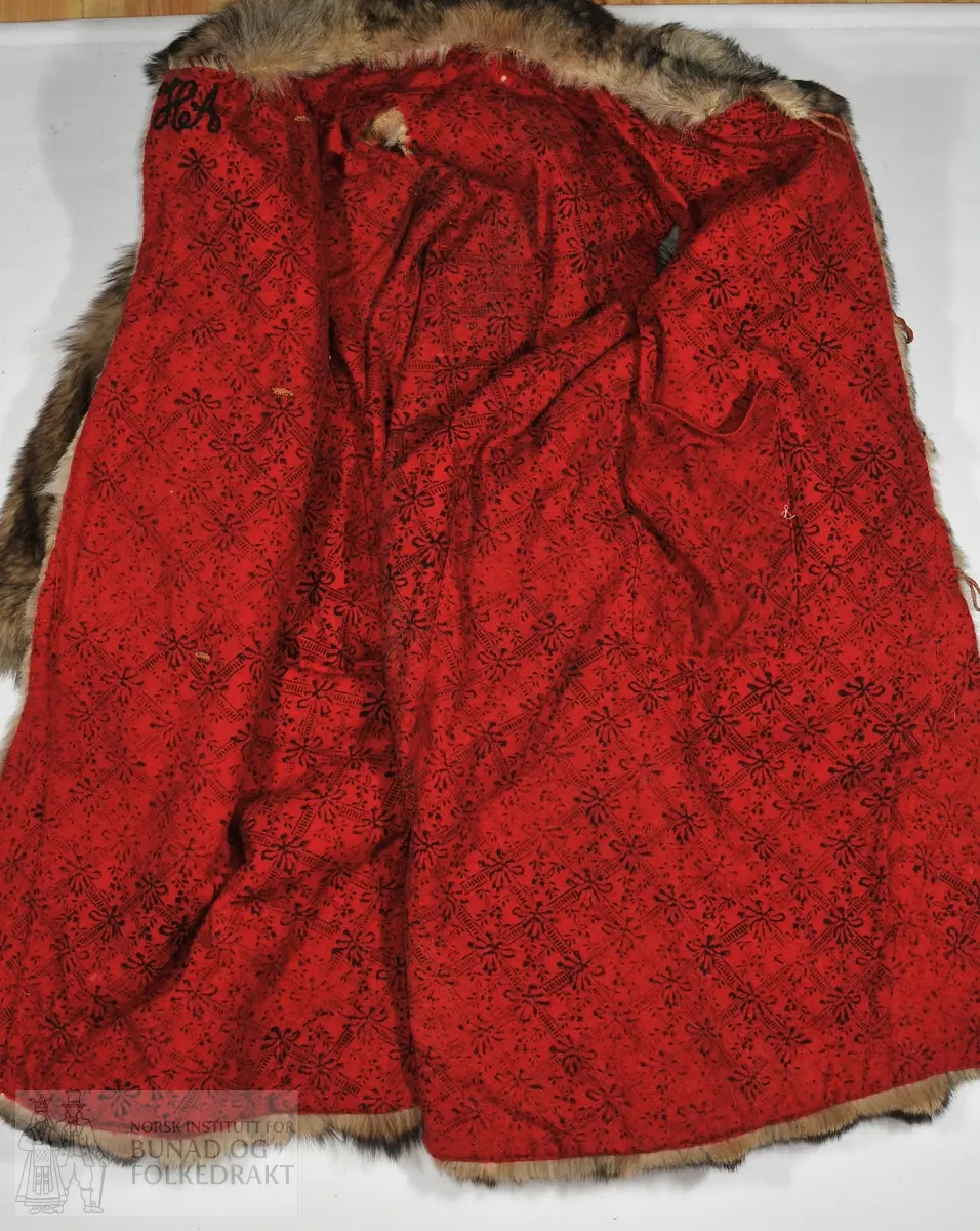 Ulveskinnspels. Brukt til lasskjøring med hest. 
Fora med raudt vove ullstoff med trykk.  Håndsydd. 

Mål: 
Krage 24cm x 30cm
Lengde rygg til nedkant 138 cm
