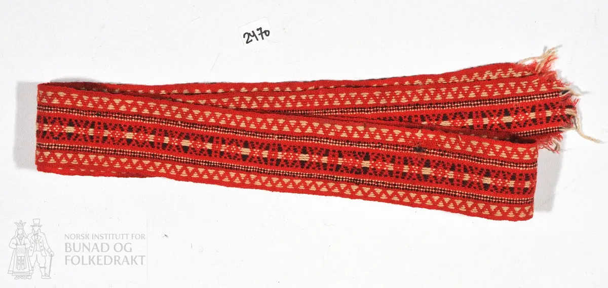 Vevd band i raud, kvit og lilla. Avrive i begge endar. 
120 cm x 4,5 cm