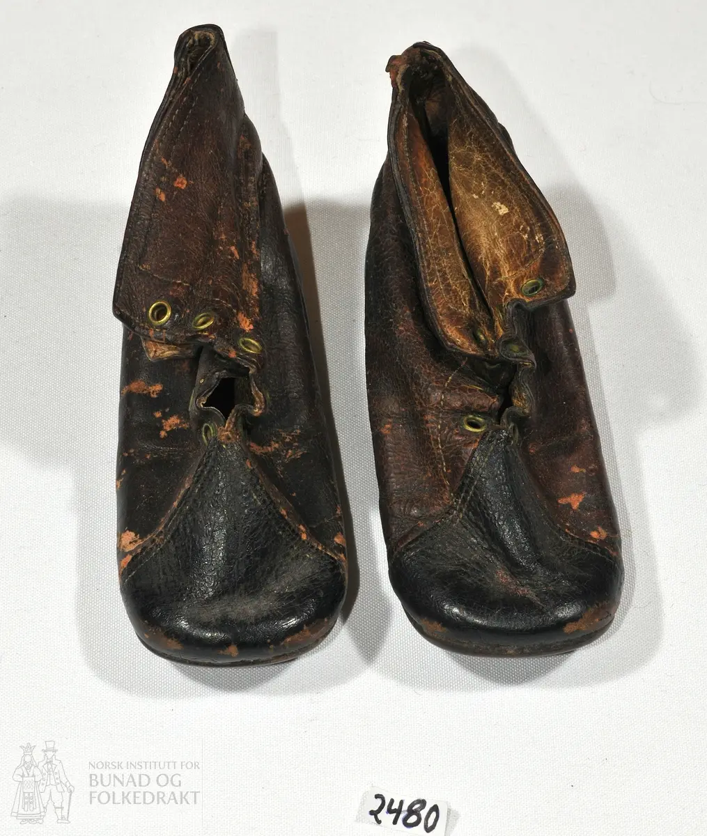 Sko av brunt skinn. 

Mål: 
Fot 14 cm. 
Høgde bak ved helen 7 cm.