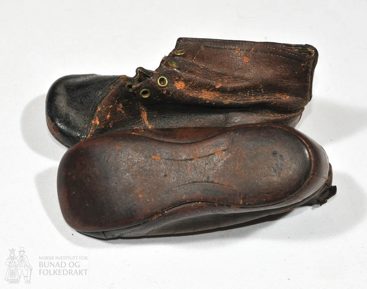 Sko av brunt skinn. 

Mål: 
Fot 14 cm. 
Høgde bak ved helen 7 cm.