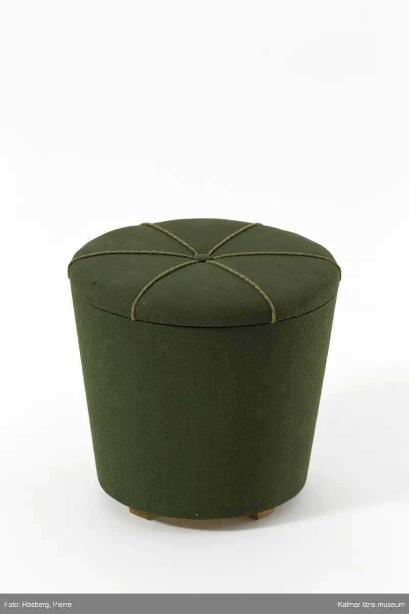 KLM 31931. Sykorg. Rund sykorg med lock. Stomme av trä, klädd i grönt bomullstyg. På locket en knapp och sex stycken virade bomullsband i ljust grön. Sykorgen har en rund insats indelad i fyra fack. Korgen innehåller garner, trådar, knappar, nålar, resårband och ett blixtlås i olika material och färger.