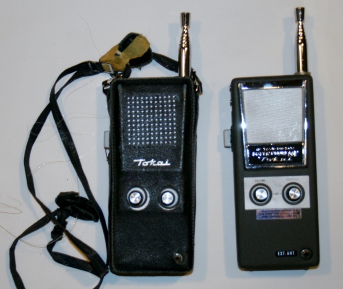 To sorte håndholdte trådløse radioer med uttrekkbar antenne. Den ene har bæreveske med stropp.