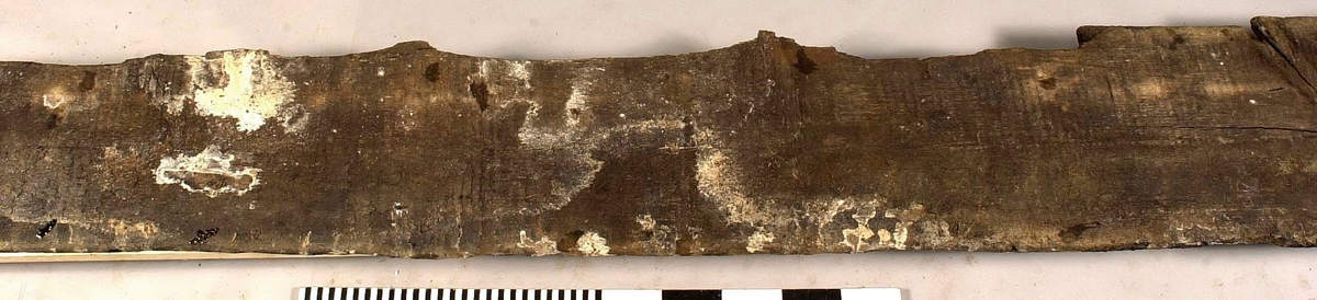 Däcksbräda.
Ena änden är skadad och partier saknas. I den andra änden börjar en genomgående spricka som löper utmed halva brädan. Skador och brott längs ena långsidan. Genomgående och ytliga sprickor.