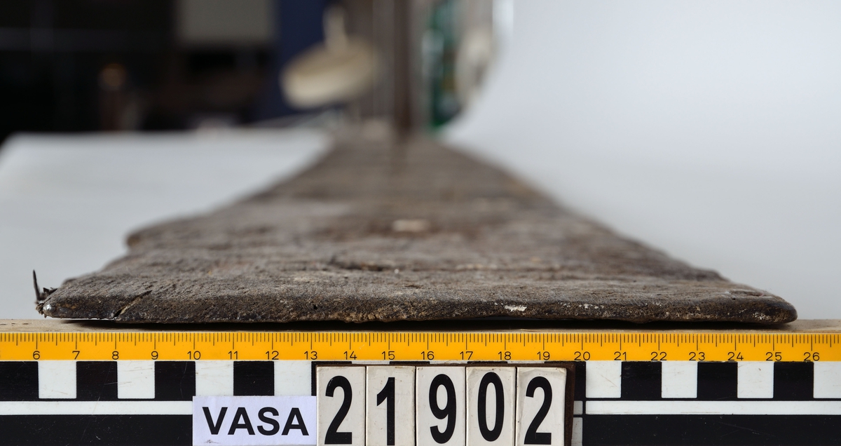 Bordplanka till mindre båt. Ena änden är runt avsmalnande vilket antyder att den har suttit mot en stäv. Den andra änden är rakt avkapad och mycket svagt fasad för att utgöra bladlask mot nästa bord. Långsidorna är nästan helt bevarade. Vid stävänden har bordets överkant ett fasat urtag för överliggande bords underkant. Spikhål längs långsidorna med vanligtvis 18-19,5 mm avstånd sins emellan. Tydliga avtryck efter spikskallar vid underkantens utsida och spår efter omböjda spik längs överkantens insida. Spikhålen är fyrkantiga med en sida på ca 4,5 mm. Fyra stycken dymlinghål fördelade längs bordets mittlinje med inbördes avstånd om ca 485-495 mm. Försänkningarna för dymlingarna på bordets utsida är kraftiga. Ytterligare ett hål sitter närmast stävänden något nedanför mittlinjen. Detta hål har en mindre diameter och har säkerligen utgjort en dyvika. Bordet har spruckit längs mittlinjen på en sträcka som överstiger något mer än halva längden. Bordet är förutom detta, och en lossbruten liten del mot ena änden, förhållandevis välbevarat. Bordets yta förefaller mer anfrätt närmare änden med lasken. Många spår efter bearbetning med yxa, speciellt mot mitten av bordplankan.
