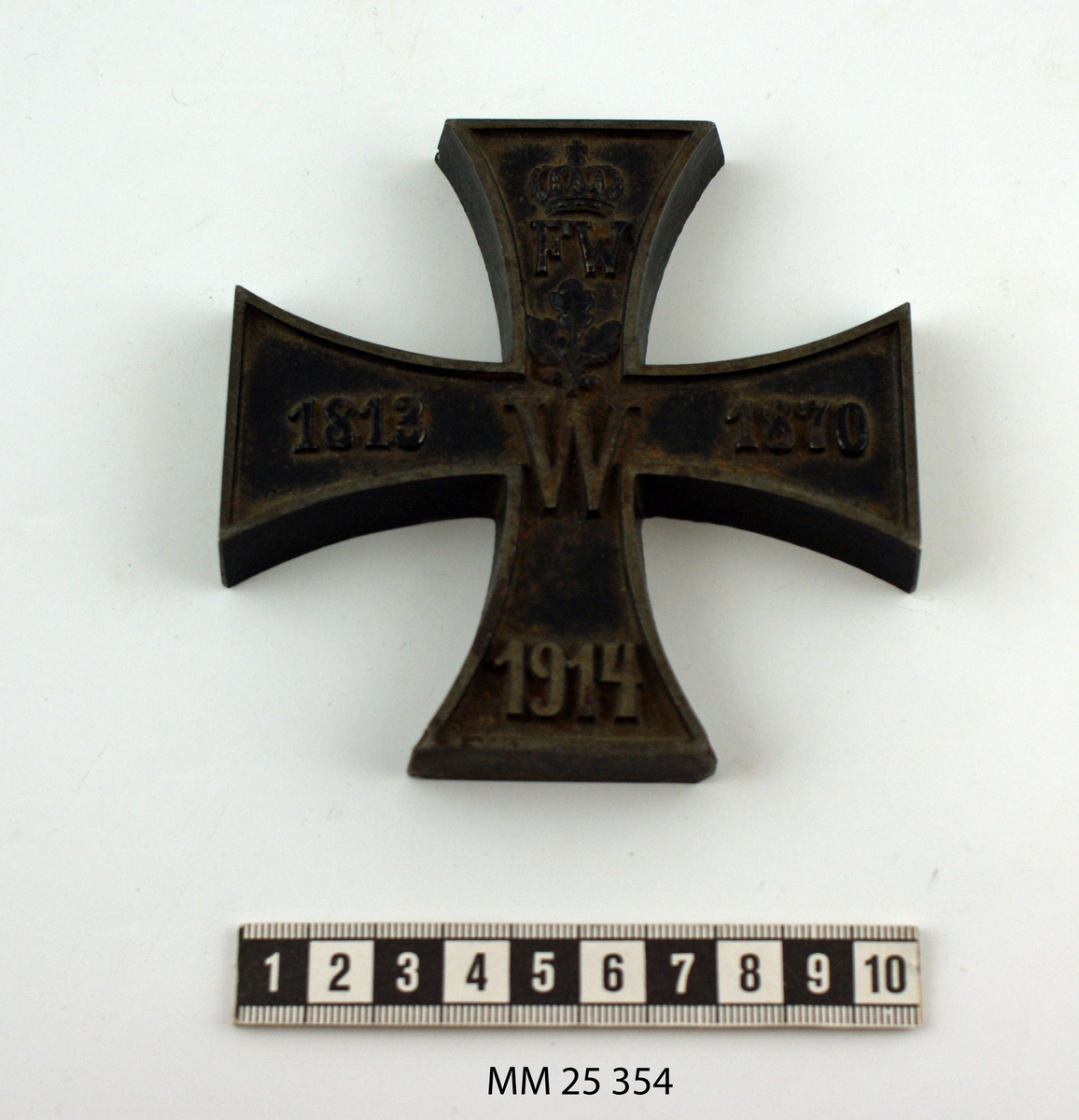 Malteserkorsformad brevpress, gjuten i metall. Runt hela kroset går en sarg som sticker upp några millimeter. I relief i korset text: "FW (under krona) W 1813 1870 1914". Mellan "FW" och "W" återfinns ett tredelat eklöv.