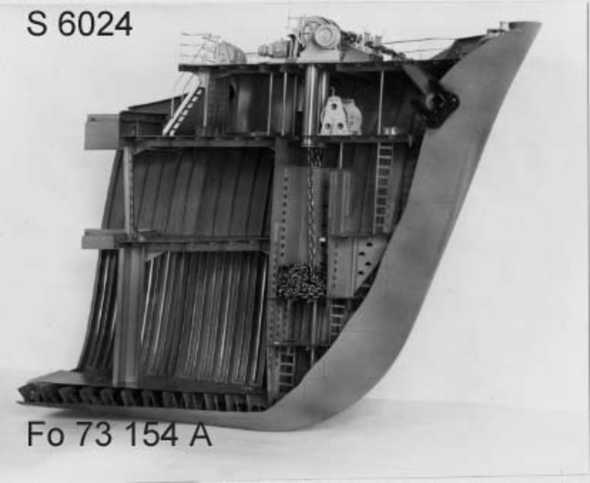 Modell av förskepp, från förstäv till mitten av l:ans lucka, byggd av metall, styrbords sida borttagen, visande konstruktionen med bottenstockar, spant, tanktak, skott och däck. Helt rödmålad. På backen gråmålat ankarspel och wirerullar. Under backen stor wirerulle. Två svarta ankare, stuvade i kättingbox.
