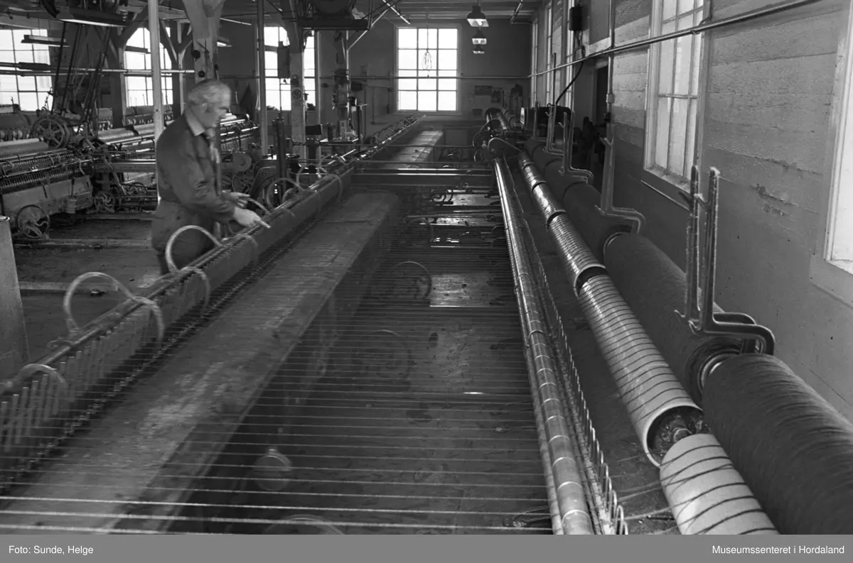 Arbeidsliv ved Salhus Tricotagefabrik i Salhus, Bergen i 1976. Arbeidar ved selfaktor (spinnemaskin) i 1900-bygget ved Salhus Tricotagefabrik.