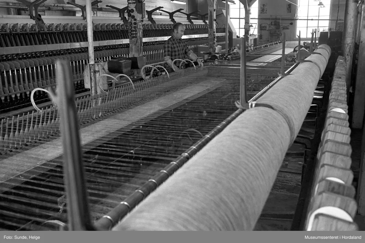 Arbeidsliv ved Salhus Tricotagefabrik i Salhus, Bergen i 1976. Arbeidar ved selfaktor (spinnemaskin) i 1900-bygget ved Salhus Tricotagefabrik.