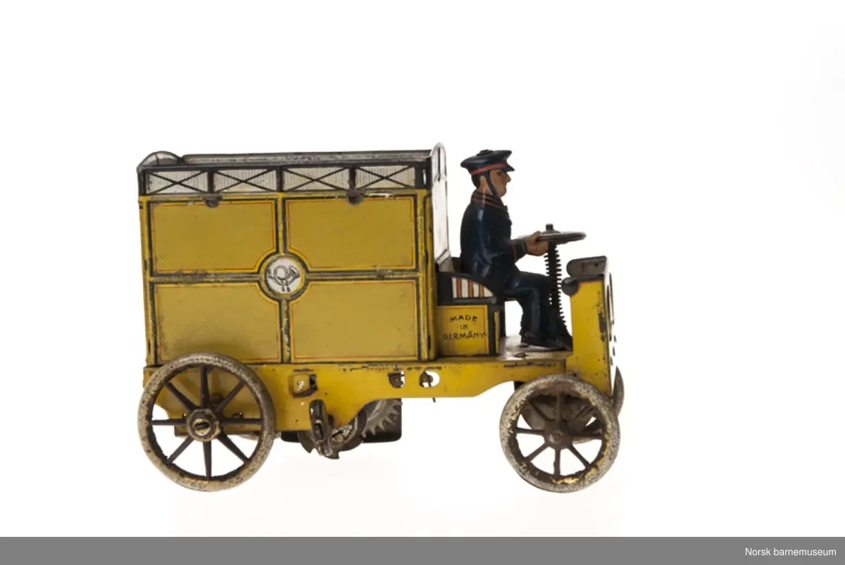 En varebil uten førerhus. Fører sitter ved rattet i blå uniform. Patentmerke med årstall fra 1903-1913 under forstellet.