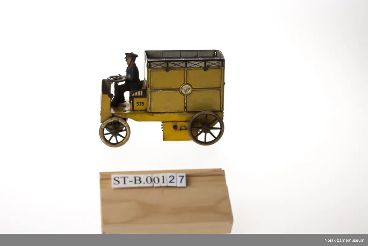 En varebil uten førerhus. Fører sitter ved rattet i blå uniform. Patentmerke med årstall fra 1903-1913 under forstellet.