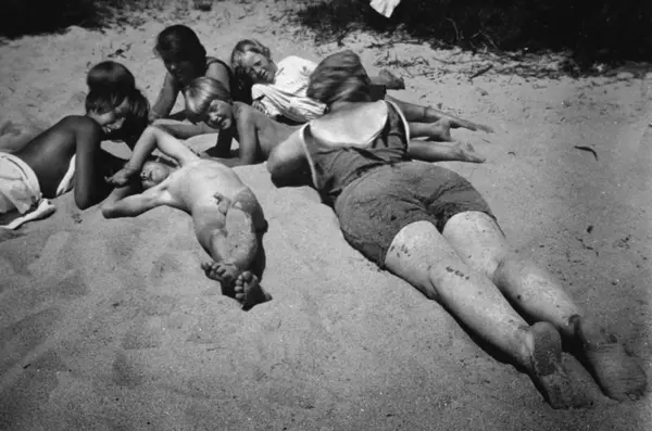 Två kvinnor och fyra barn ligger och solar på sanden, trolig