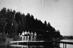 Två pojkar och fem badklädda män poserar ståendes på en bryg