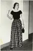 Nordiska Kompaniet. Tonårsmode 1950. Flicka i lång, rutig kjol och kortärmad svart jumper (sannolikt angora.) Svart skärp i midjan. Text på baksidan: 1950.