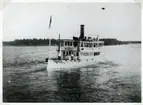 Fartyget lämnar Ekuddens brygga vid Vaxholm. I bakgrunden ligger Ekholmen och till höger ser man Tenösund. Gåva av Gunnar Hellström.