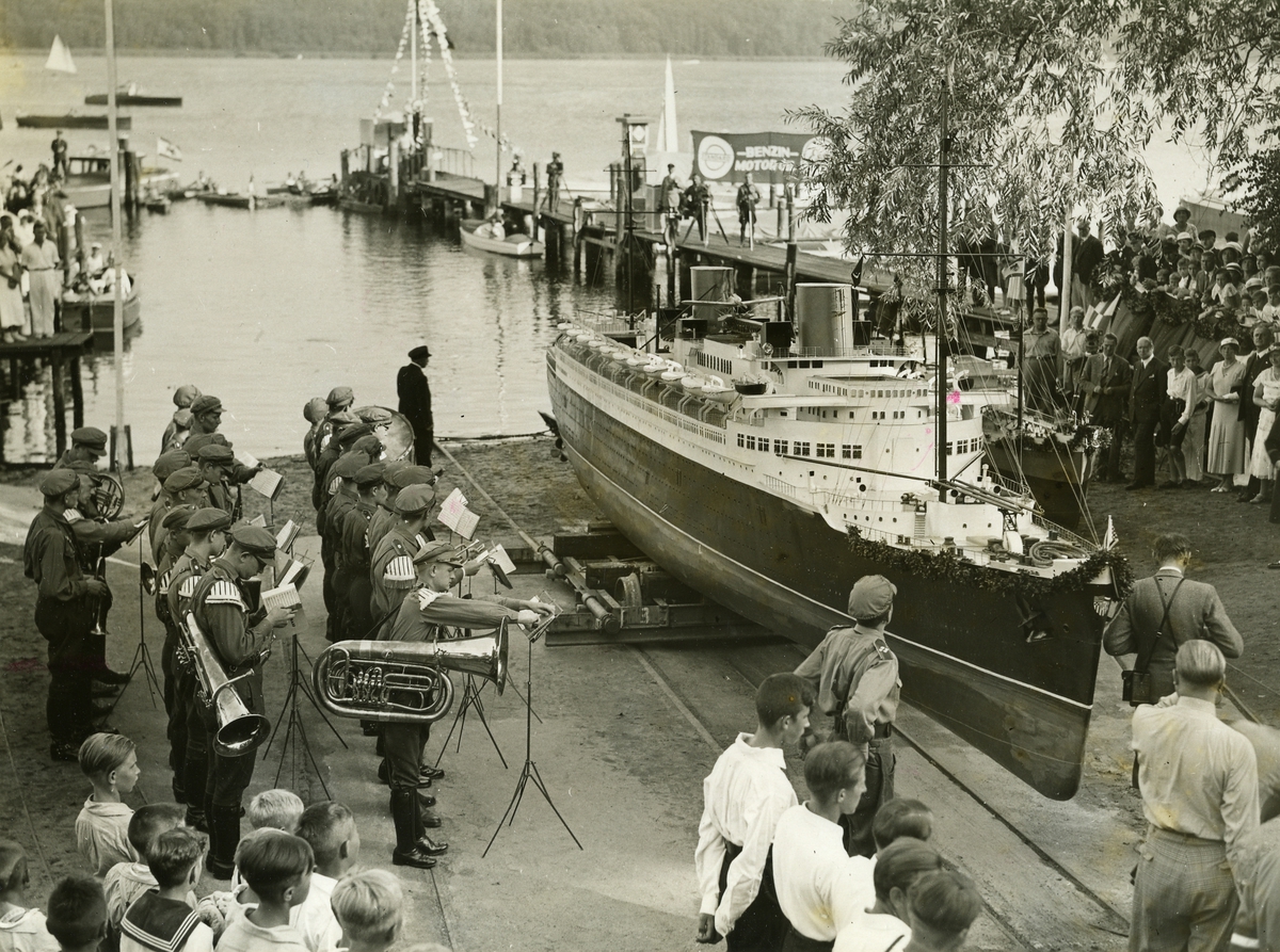 Skeppsmodell-Byggnadsskola.
"STAPELLAUF DER KLEINEN "BREMEN". eE 9232/1. Potsdam. An Templiner See in Potsdam besteht seit 8 Jahren eine Schiffsmodell-Bauschule, in der eine ganz Flotte von nachgebildeten Dampfern und Seglern an Anker liegt. Alle Modelle werden im Masstab 1:20 angefertigt und sind den Orginal bis in das kleinste Detail nachgebildet..- Am feierlichen Stapellauf der Nachbildung der "Bremen", der am 17.August abgehalten wurde, war Reichsjugend führer Baldur von Schirach persönlich anwesend. Undser Bild zeigt die Schüler der Modellbauschule in der Uniform der Hitlerjugend bei der feierlichen Taufe der Miniatur "Bremen". Trotz des Masstabes ist der Bau sehr ansehnlich, wie auf dem Bild in Vergleich zu der Grösse der Jungen ersichtlich.
PHOTO NEW YORK TIMES BERLIN Text ohne Gewähr 33818Bö70".
