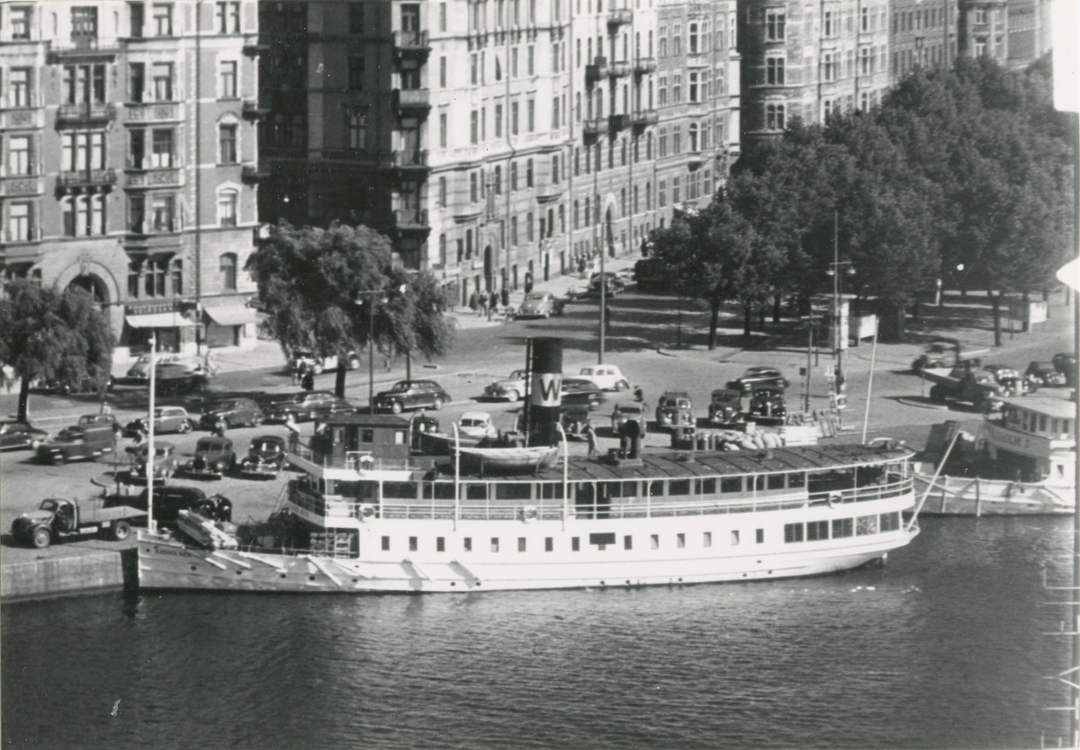 Foto i svartvitt visande passagerarångfartyget Kanholmen av Vaxholm vid kaj, Strandvägen vid Nybroplan.