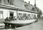 Folk samlade vid segelbåt under byggnad, på gården till huset Söder Mälarstrand 10-12 Segelbåtar byggdes i en källare på gården. En sådan båt var t.o.m. med i kappseglingar och vann pris. Foto omkr. 1911-1912.