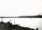 Fotot taget i skymningen från Sandins föräldrahem Söder Mälarstrand 10 - 12, med utsikt över Riddarfjärden. I förgrunden S. Mälarstrands kaj. Omkring 1918-20.