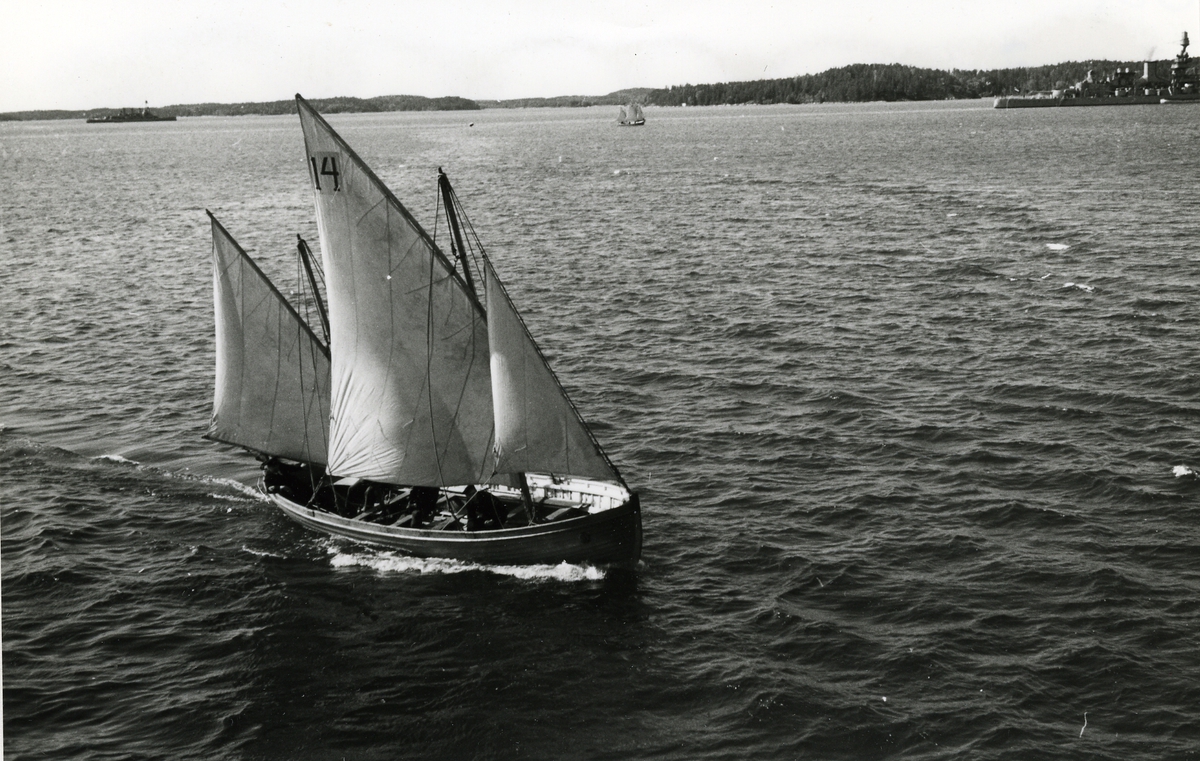 Kappseglande båt, troligen på Hårsfjärden i Stockholms skärgård. I bakgrunden pansarskeppen Gustaf V och Oscar II.