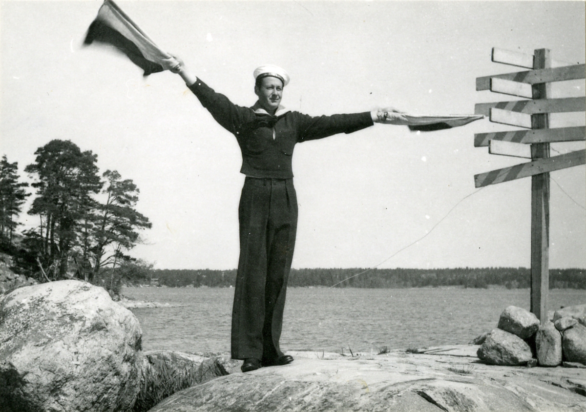 En man från jagaren Stockholm med semaforflaggor på land.