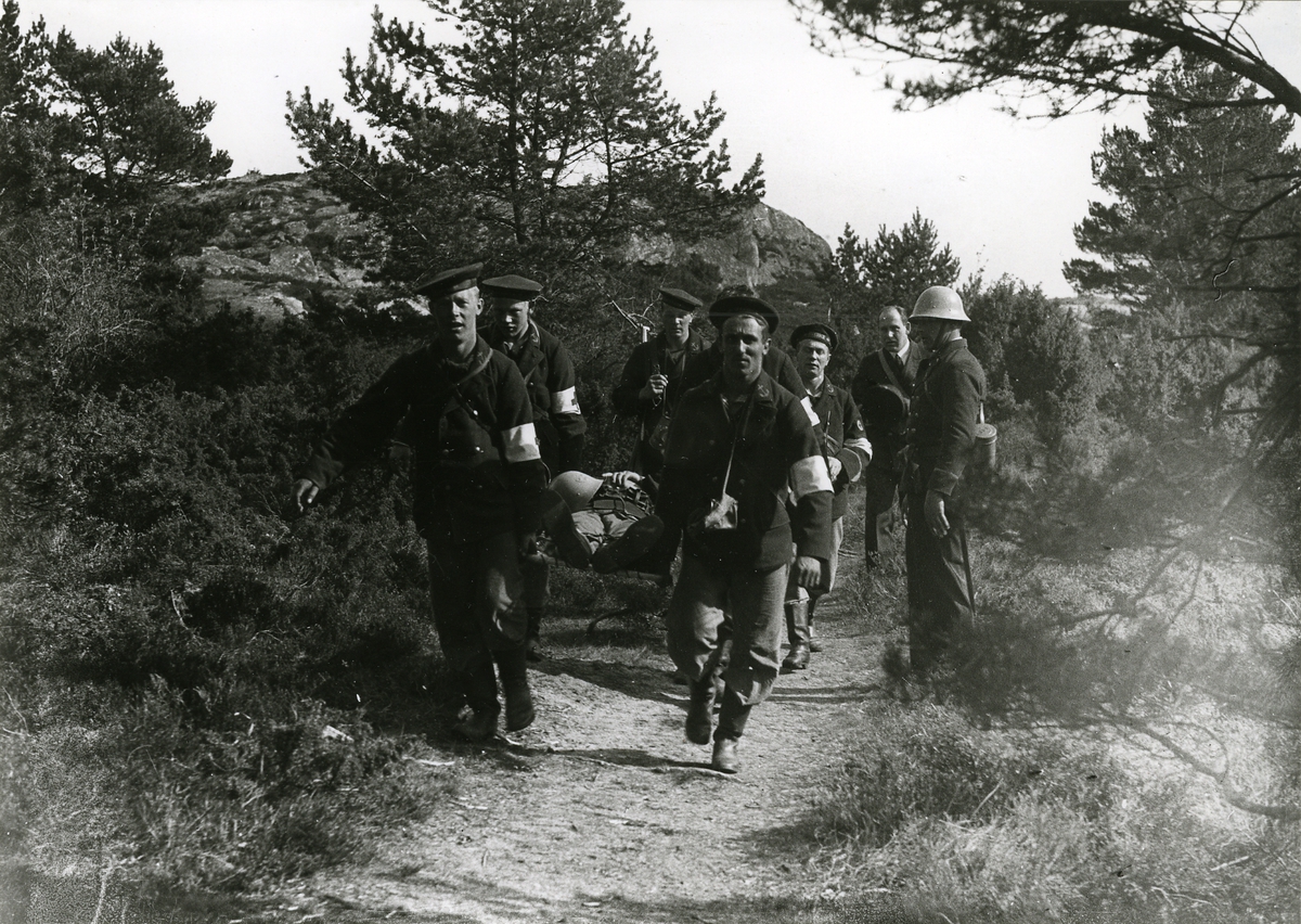 Besättningsmän från pansarskeppet Sverige bär en man på bår vid manöver på skärgårdsö.