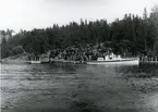 Landsatt manskap på strand. Motorbarkass i förgrunden.