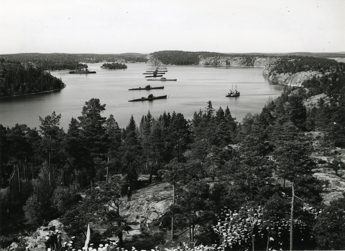 Ubåtar av typ Hajen och depåfartyget Svea till ankars i skärgården.
I förgrunden manskap samlat på land.