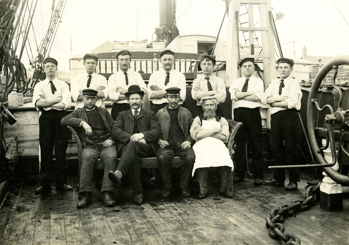 [från fotobeskrivningen:] "3-mast barkskeppet BERTHA av Vätö, b. 1874. Gruppbild av besättningen, 1906. Sittande från vänster: Konstapel Emanuel Pettersson, Rådmansö Kapten J. A. Pettersson, Björkö-Arholma Styrman Theodor Pettersson, W. Edsvik Steward Mattsson, 'Back-Matte'. Stående från vänster: Wärnberg, Wisby Malmöpojken Sverre Högmarsöpojke Högmarsöpojken Carlsson Mattsson, Högmarsö, timmerman Mattsson, bror till stewarden Matsson, bror till timmerman."