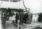 Pontonkajen till sportutställningen år 1905 vid Djurgårdsbrunnsviken. Prins Wilhelm i regn och keps. I bakgrunden Waterloo med flagga.