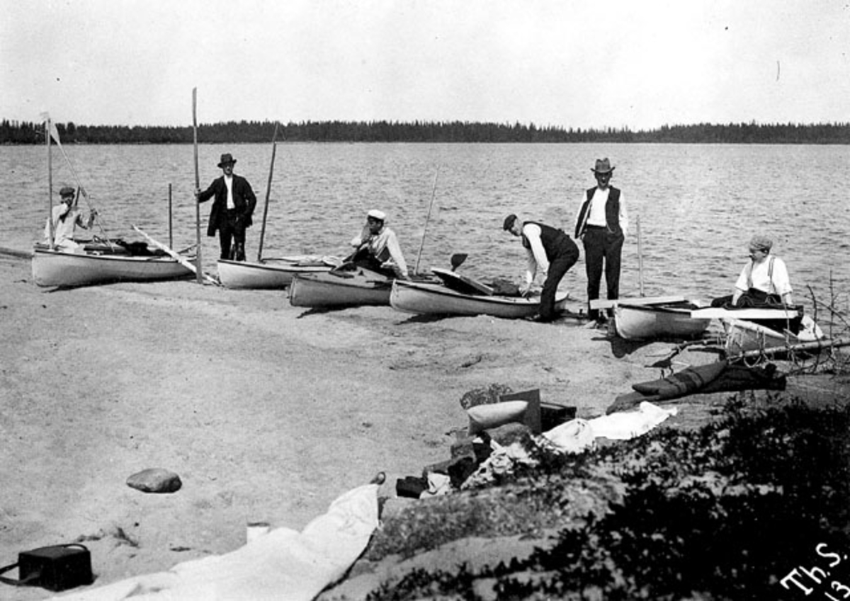 Kanotister med paddelkanoter på strand.