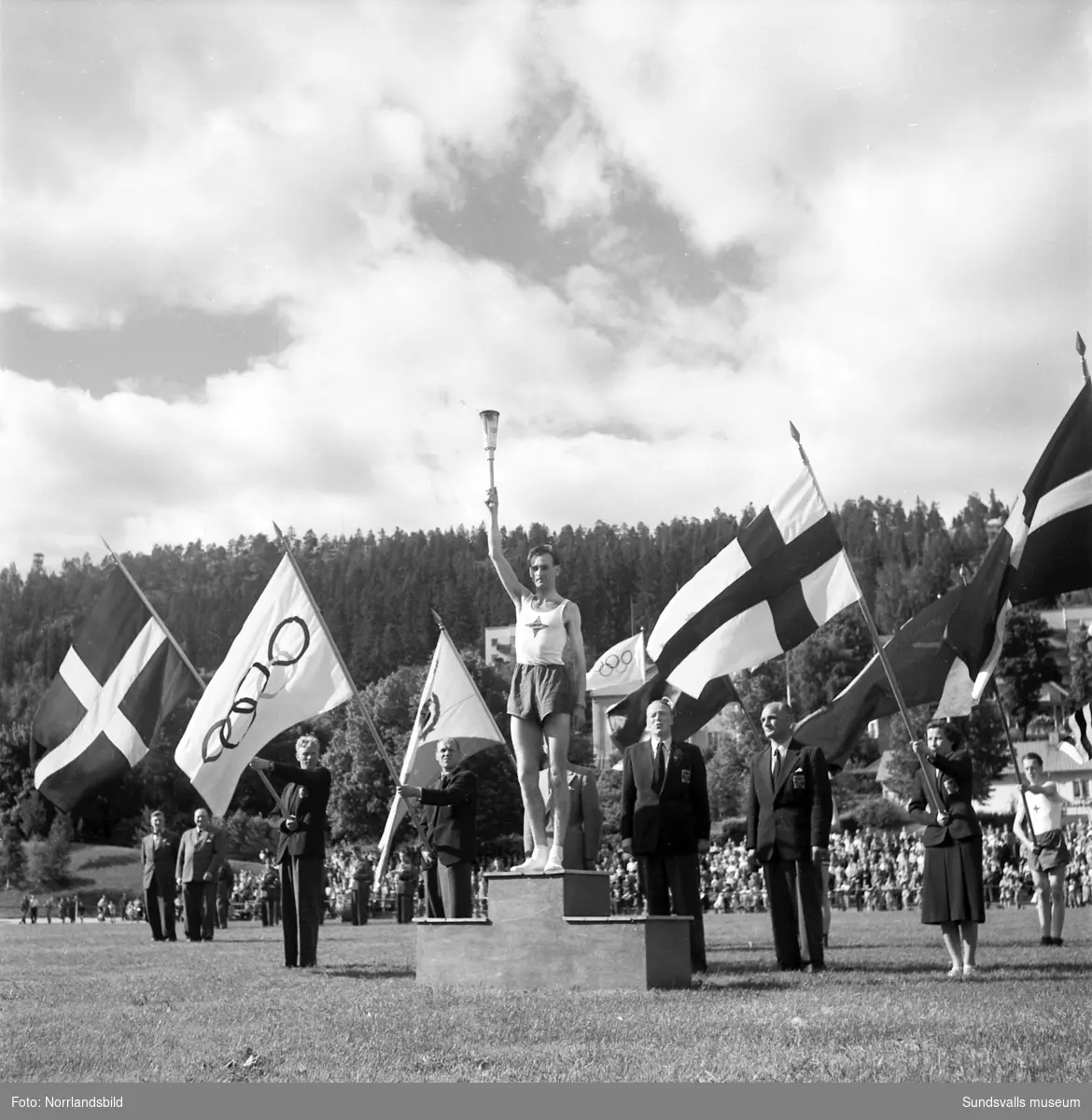 Den olympiska elden passerar Sundsvall inför sommarspelen i Helsingfors 1952 med högtidlig stafettväxling i Idrottsparken. In på arenan förs facklan av IFK-löparen Eric Nilsson, som är uttagen till Olympiaden på 3000 meter hinder. Därefter tar SAIK-brottaren och OS-silvermedaljören från 1936, John Nyman över för att påbörja facklans färd vidare mot Härnösand och Kramfors.