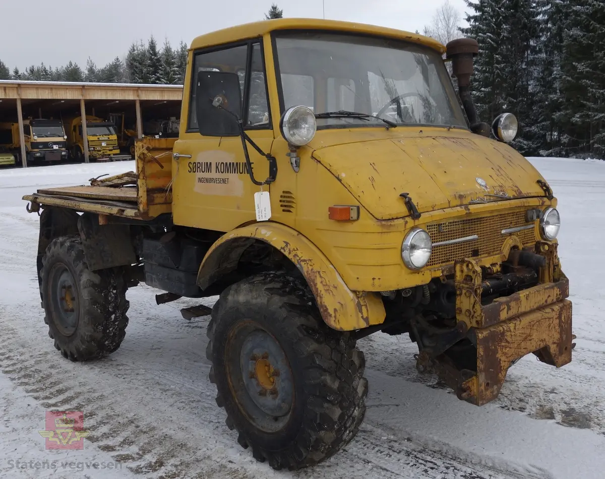 MB Unimog 406. Lastebil på 4 hjul, (to akslet), med akselavstand 240 cm. I hovedsak gul. 4-hjuls drift. Kjøretøyet har for fremdrift en 6-sylindret dieselmotor, antatt av typen M.B OM 352 X 11 fra Mercedes Daimler Benz. Motoren yter 84 Hk (61,76 KW) og har et slagvolum på 5700 kubikkcentimeter.
Schmidt standard frontmontert redskapsfeste. Antall seter er 2. Standard dekkdimensjon skal være 12,5-20 rundt om.