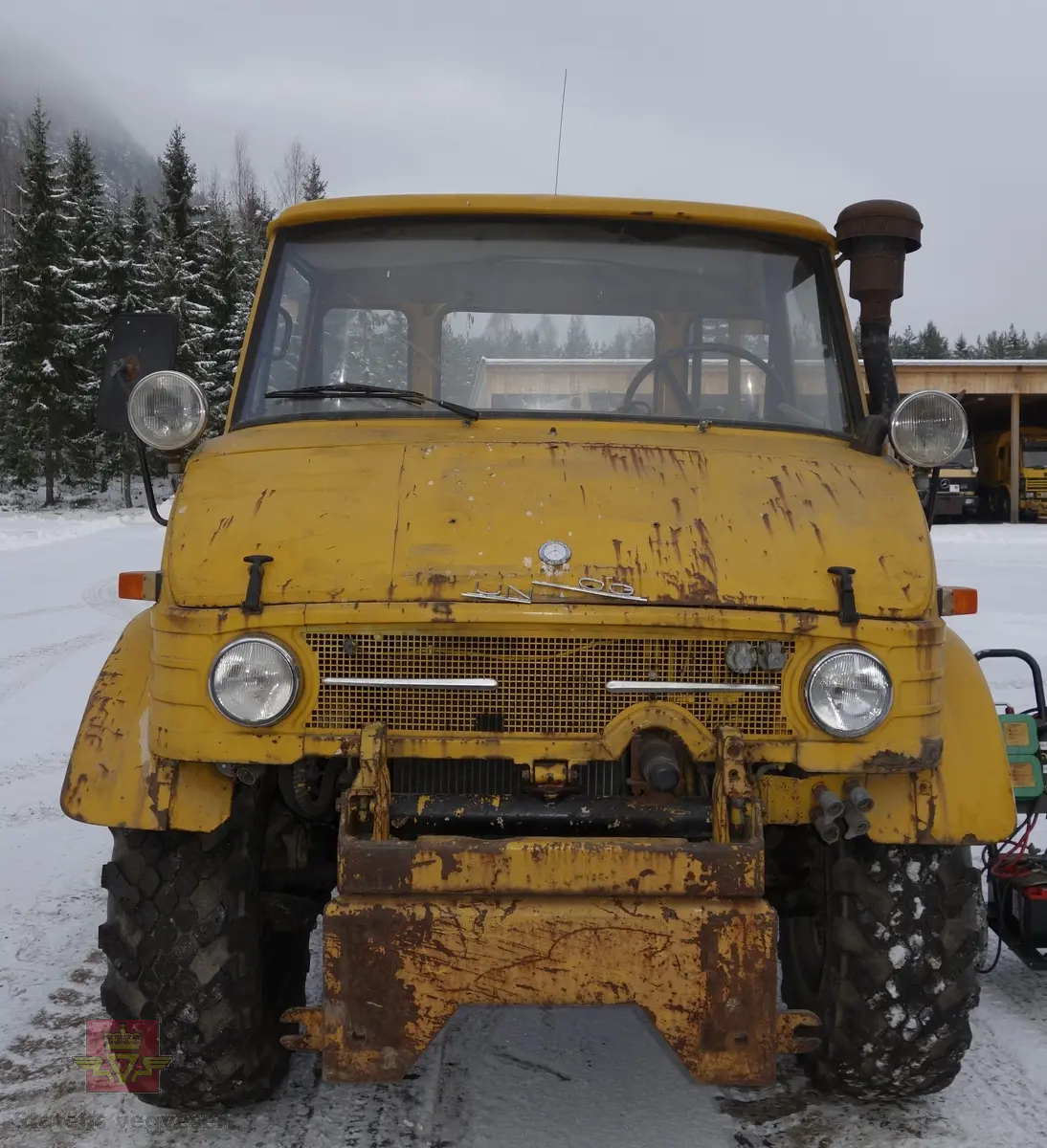 MB Unimog 406. Lastebil på 4 hjul, (to akslet), med akselavstand 240 cm. I hovedsak gul. 4-hjuls drift. Kjøretøyet har for fremdrift en 6-sylindret dieselmotor, antatt av typen M.B OM 352 X 11 fra Mercedes Daimler Benz. Motoren yter 84 Hk (61,76 KW) og har et slagvolum på 5700 kubikkcentimeter.
Schmidt standard frontmontert redskapsfeste. Antall seter er 2. Standard dekkdimensjon skal være 12,5-20 rundt om.