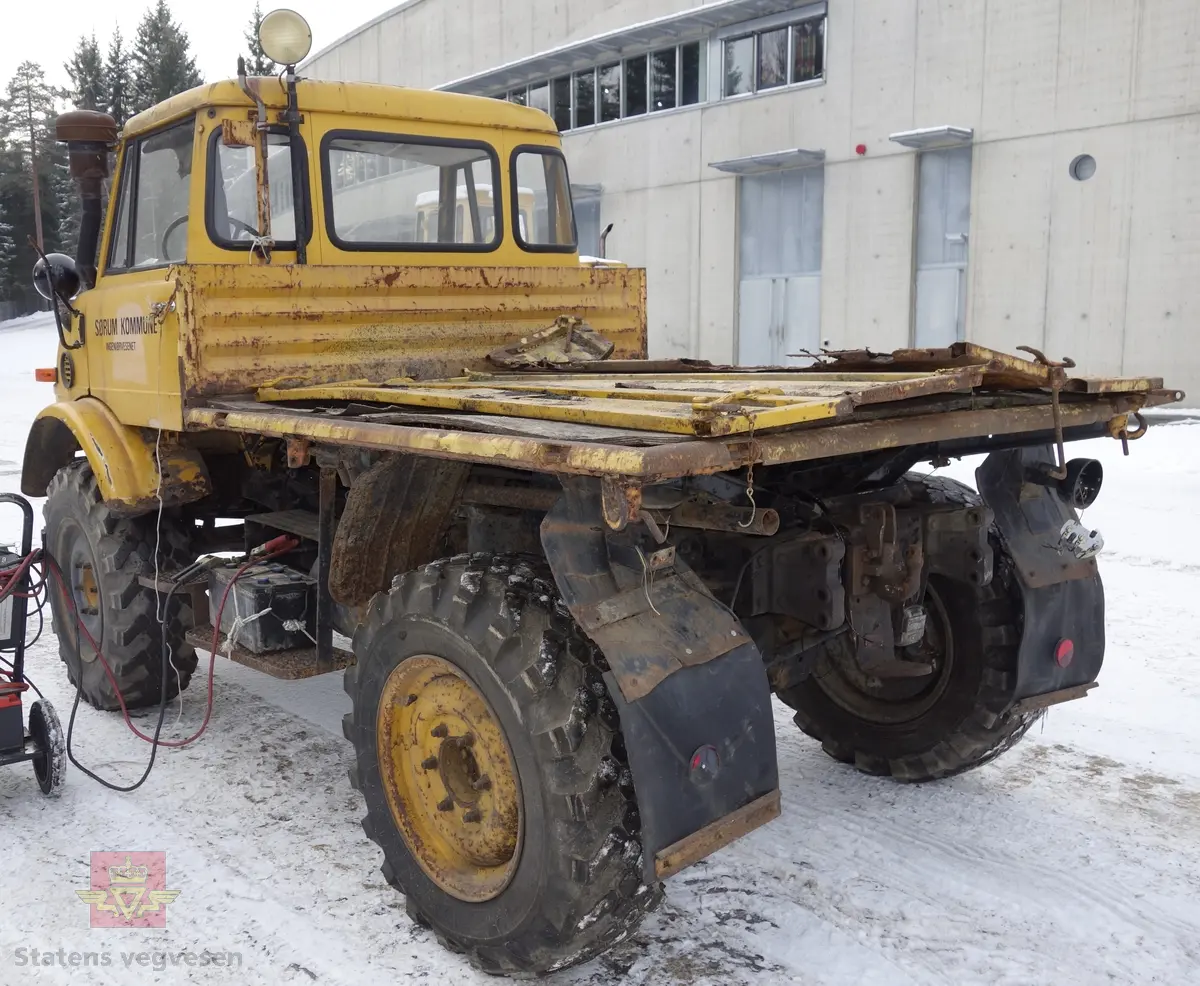 MB Unimog 406. Lastebil på 4 hjul, (to akslet), med akselavstand 240 cm. I hovedsak gul. 4-hjuls drift. Kjøretøyet har for fremdrift en 6-sylindret dieselmotor, antatt av typen M.B OM 352 X 11 fra Mercedes Daimler Benz. Motoren yter 84 Hk (61,76 KW) og har et slagvolum på 5700 kubikkcentimeter.
Schmidt standard frontmontert redskapsfeste. Antall seter er 2. Standard dekkdimensjon skal være 12,5-20 rundt om.