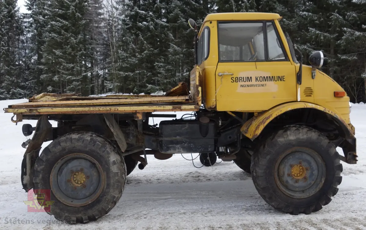 MB Unimog 406. Lastebil på 4 hjul, (to akslet), med akselavstand 240 cm. I hovedsak gul. 4-hjuls drift. Kjøretøyet har for fremdrift en 6-sylindret dieselmotor, antatt av typen M.B OM 352 X 11 fra Mercedes Daimler Benz. Motoren yter 84 Hk (61,76 KW) og har et slagvolum på 5700 kubikkcentimeter.
Schmidt standard frontmontert redskapsfeste. Antall seter er 2. Standard dekkdimensjon skal være 12,5-20 rundt om.