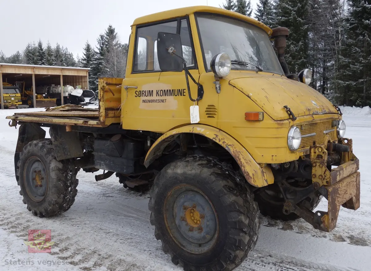 MB Unimog 406. Lastebil på 4 hjul, (to akslet), med akselavstand 240 cm. I hovedsak gul. 4-hjuls drift. Kjøretøyet har for fremdrift en 6-sylindret dieselmotor, antatt av typen M.B OM 352 X 11 fra Mercedes Daimler Benz. Motoren yter 84 Hk (61,76 KW) og har et slagvolum på 5700 kubikkcentimeter.
Schmidt standard frontmontert redskapsfeste. Antall seter er 2. Standard dekkdimensjon skal være 12,5-20 rundt om.