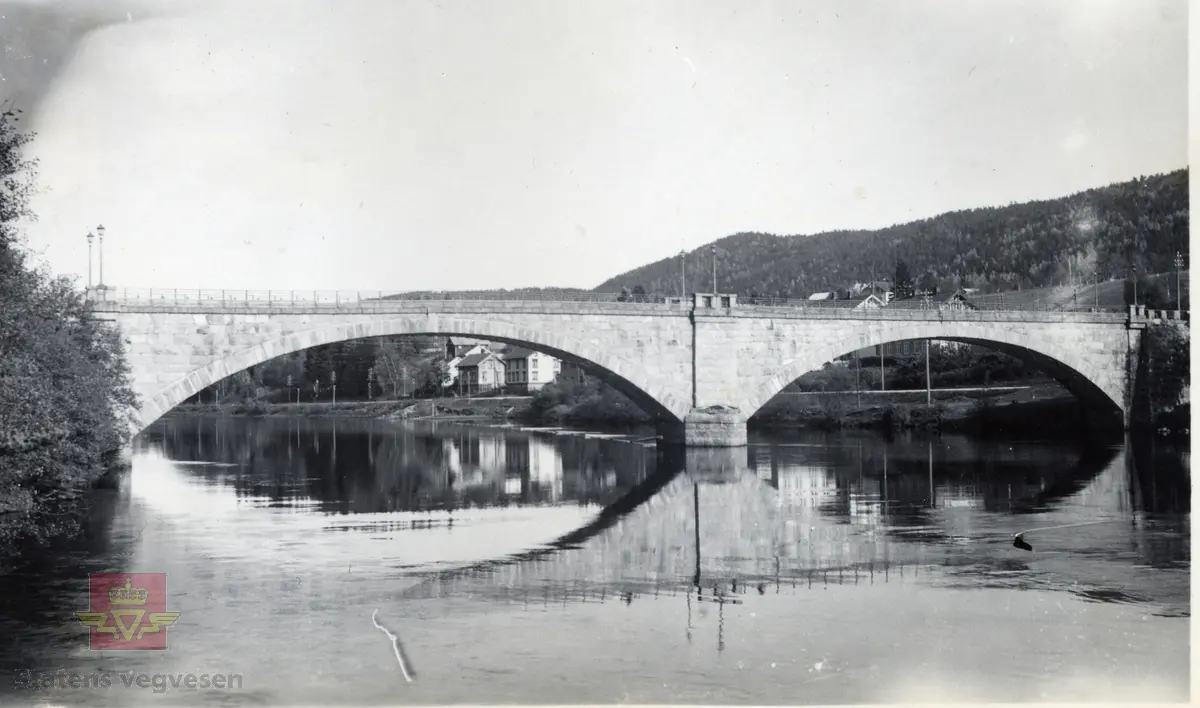 Steinhvelvbru med to spenn. Sannsynligvis Åmfoss bru - gamle Åmli bru over Nidelva i Åmli kommune, bygd 1918, jr. "Nasjonal verneplan for veger, bruer og vegrelaterte  kulturminner, Statens vegvesen - Region Sør".