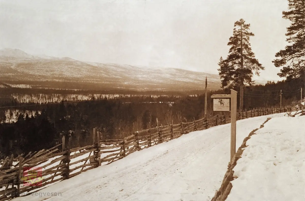 "Veianlæg". "Ved Aune i Opdal". Bildet er tatt ved Stuen skysstasjon på Nordskogen i Oppdal, og med bildet av riksvåpenet  på skiltet.