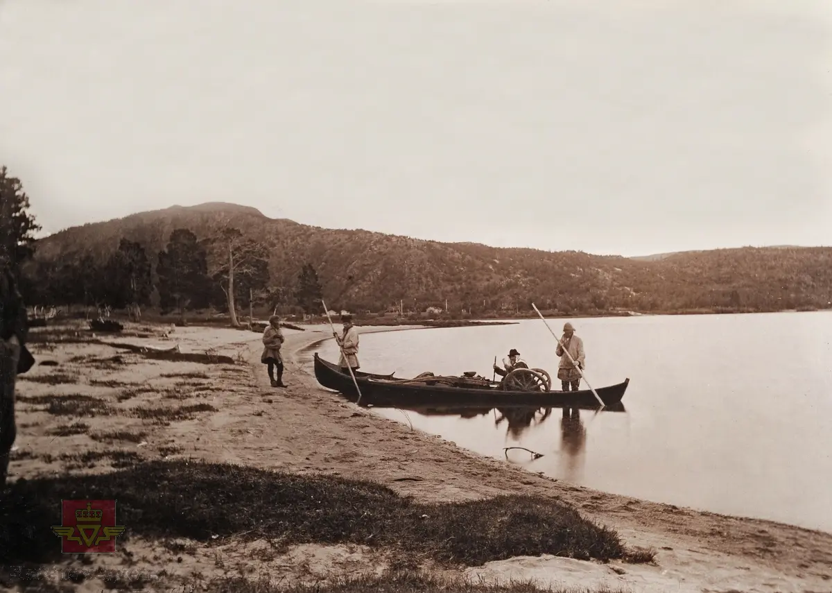 "Veianlæg". "Skoganvarrevand". Personen sittende i båten er  sannsynlig Hans Hagerup Krag som var vegdirektør 1874 - 1903, han bærer et hodeplagg som beskytter spesielt mot mygg. Tre samer i følge.