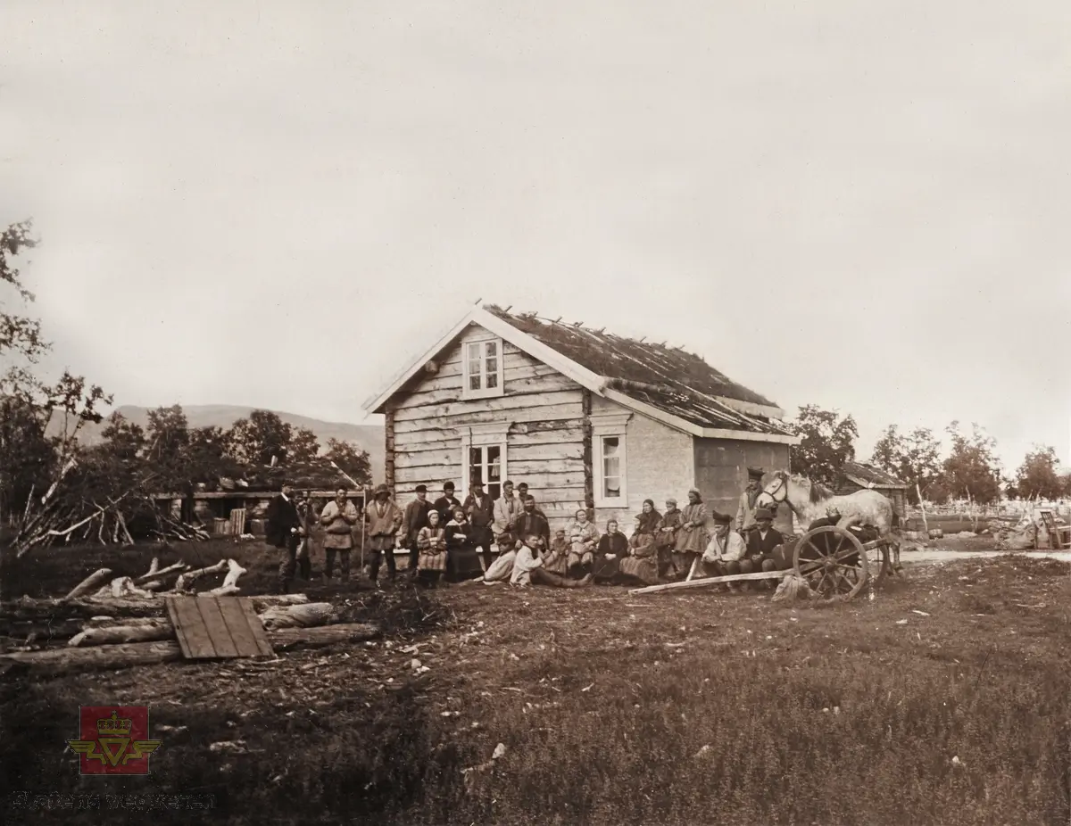 "Veianlæg". Ei gruppe av samer og tilreisende med hest og kjerre  utenfor et tømret hus.

Dette er Ildskog i Lakselv. Fjellet i bakgrunnen på bildet er ikke til å ta feil av. 
(Opplysninger fra Tone M. Andersen)