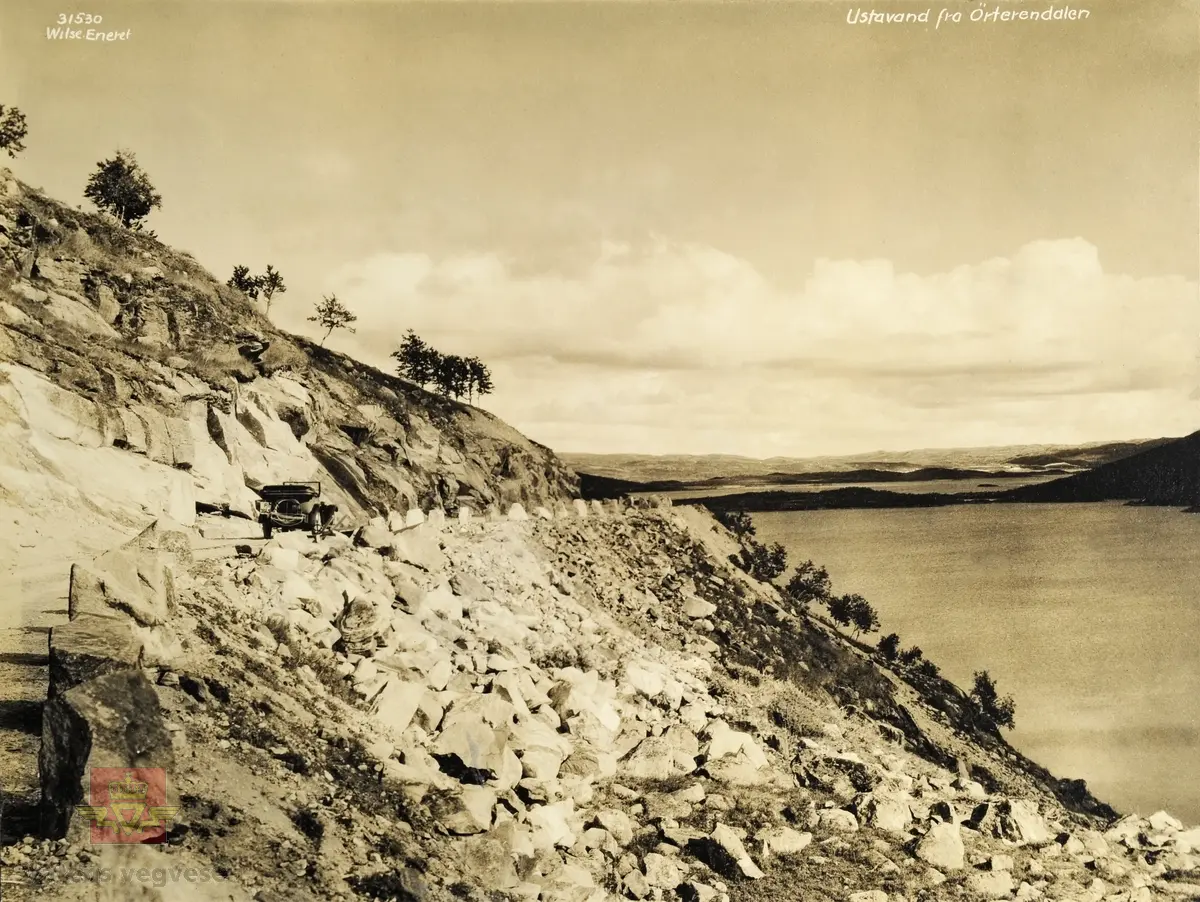 "Veianlæg". Bildet er merket: "Ustadvand fra Örterendalen ". Nr. 31530.  Eneret. Wilse. 
Bil med kjennemerke F 3645. "Stasjonsmester Johan Sæther på Haugastøl hadde en Buick på reg. nr. F-3645.  Den var registrert som drosje.  Ifølge Bilboken for Norge 1927 og 1929." Sannsynligvis  samme bil og bildemotiv  som NVM 00-F-32360 og NVM 00-F-32362.