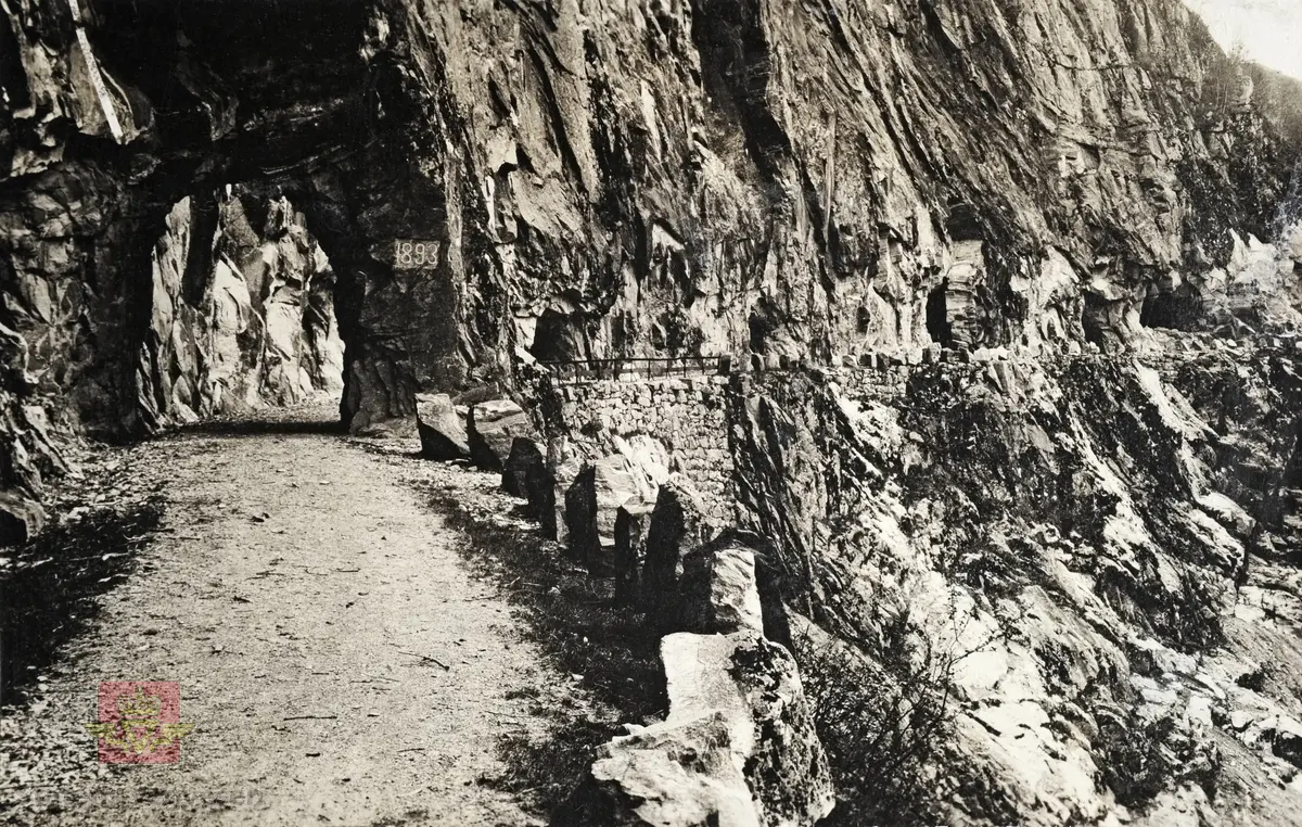 "Veianlæg". "Bergsdalsveien i Hordaland." Dette er vegen til Bergsdalen som ble bygd på 1890-tallet. Tunnel i fjellet med stabbesteinsrekkverk etter vegen, og rekkverk av bjelker over tørrmuren.  På et skilt i fjellveggen står det 1893.