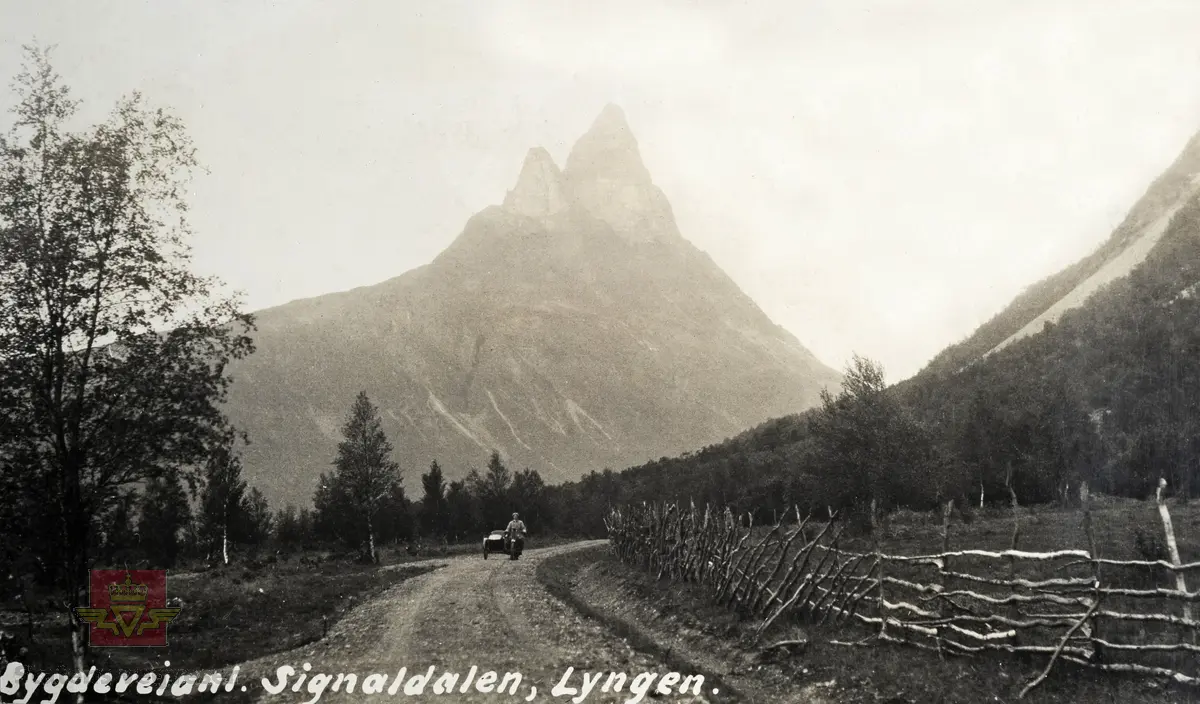 "Veianlæg". "Bygdeveianl. Signaldalen".  Motorsyklist med sidevogn.  I bakgrunnen ruver Otertind med sine 1354 moh. Gjerdet/hafelle er av fjellbjørk.